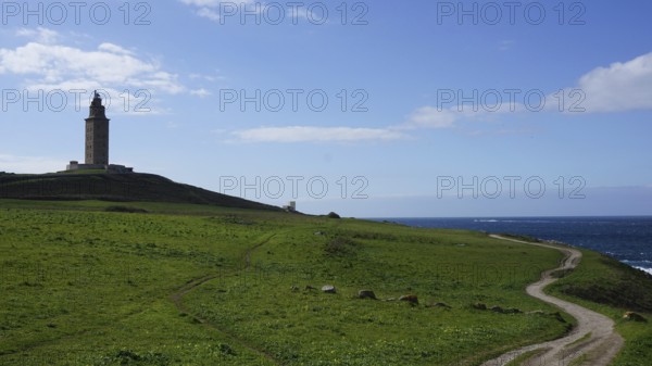 Coast with lighthouse and green field under a blue sky with clouds and a path to the sea, A Coruna,