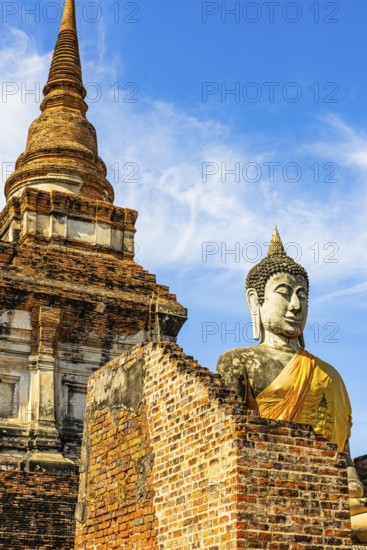 Stone Buddha statue decorated with yellow cloth, in the back a high temple tower, Prang, historic