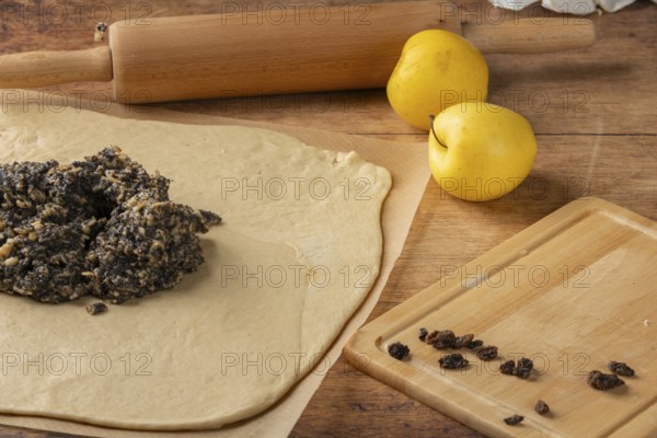 Rolled dough with poppy seeds and raisins on top, apple and rolling pin next to it