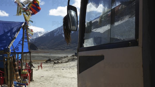 A bus and a colorful tent with pennants against a mountain backdrop, snack at a kiosk on a plateau