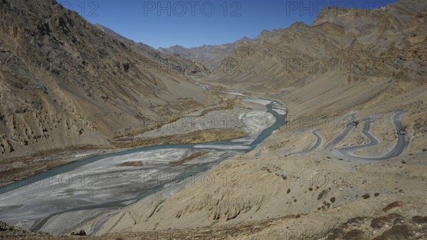 Shimmering blue Indus meanders through a barren valley with serpentines of a road leading down to