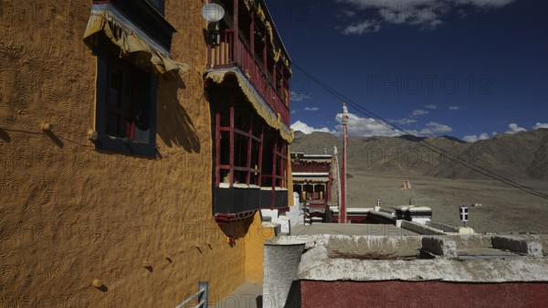 Façade of a Buddhist monastery casting shadows against a clear sky and mountain landscape, trekking