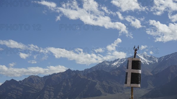 Mountain landscape with blue sky and clouds, flag in the foreground, trekking in Ladakh, Himalayas,