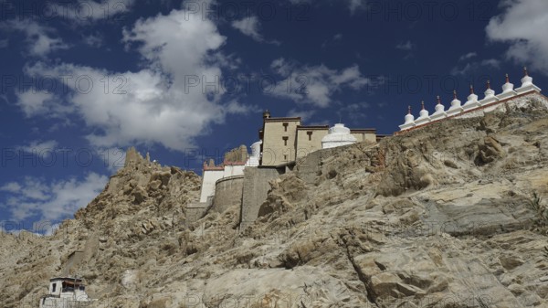 Buddhist monastery on a rocky slope under a bright blue sky with white clouds, trekking in Ladakh,
