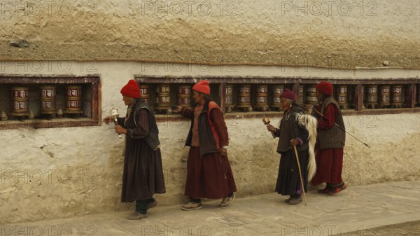Four believers in traditional clothing turn a series of prayer wheels along the old wall of a