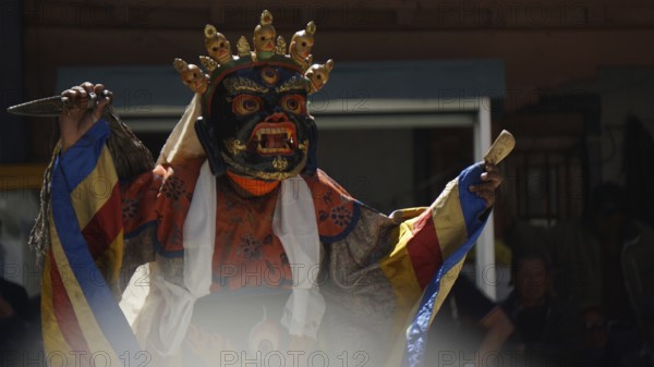 A mystical, colorfully dressed dancer wears a decorative mask during a ritual, Leh, trekking in