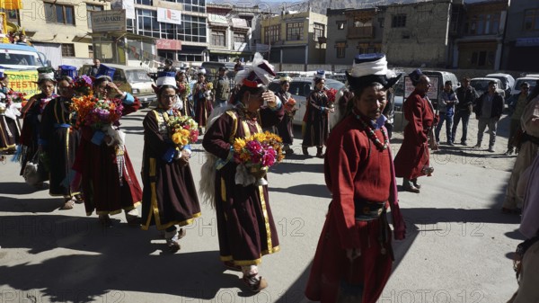 People wearing traditional garments carry flowers during a festive procession in Leh, trekking in