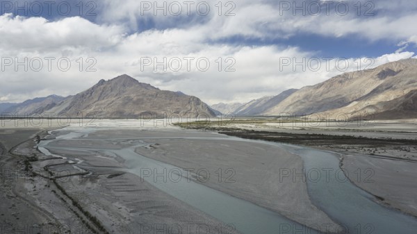Extensive river landscape on the Indus with mountains in the background under a cloud cover,