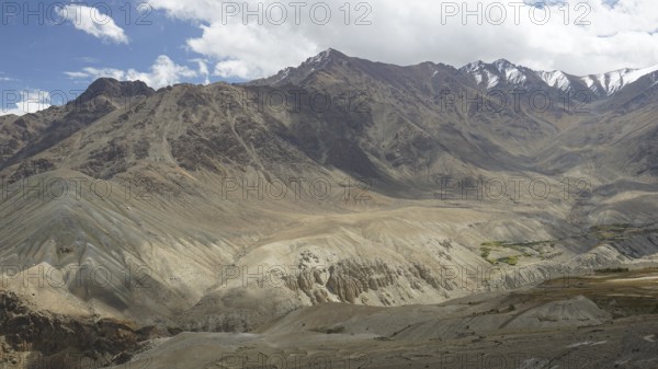 Dramatic mountain landscape with diverse rock formations, snow-capped peaks under a cloudy sky,