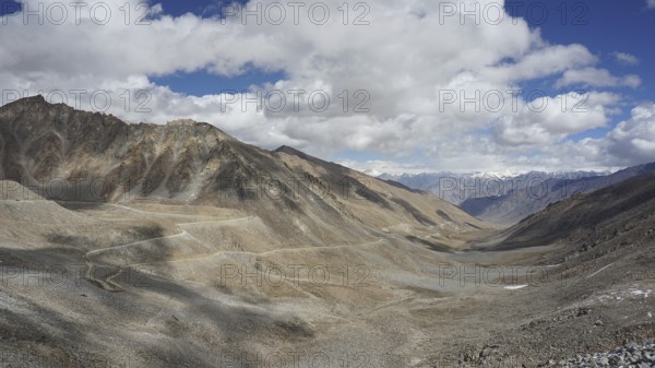 Wide mountain landscape with winding mountain road under a cloudy sky, trekking in Ladakh,