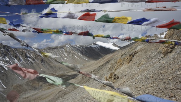 Colourful prayer flags waving in the wind against an impressive mountain landscape under partly