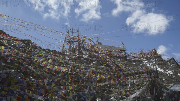 A network of colorful prayer flags stretched at Khardung-La Pass under a blue sky, trekking in