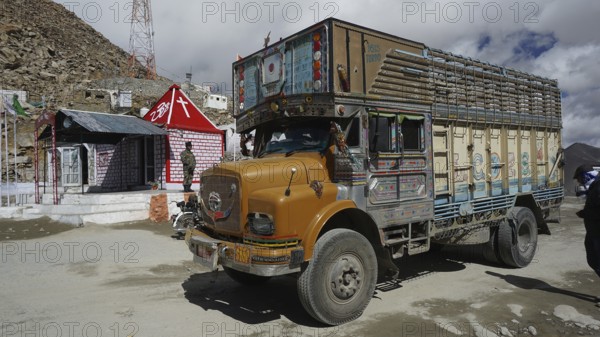 Colourful truck at Khardung-La Pass next to other vehicles and small houses with Indian flag under