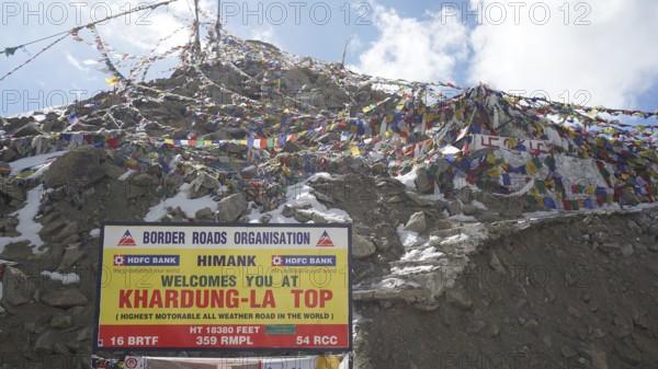 Colourful prayer flags fly next to the Khardung-La Top sign on the summit, trekking in Ladakh,