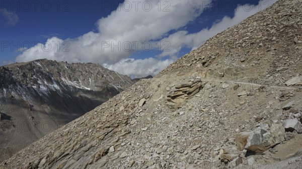 Rocky mountain terrain with road on the mountainside under a sunny sky with scattered clouds,