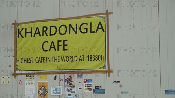 Sign of a cafe at Khardungla Pass on a high mountain road with various stickers, trekking in