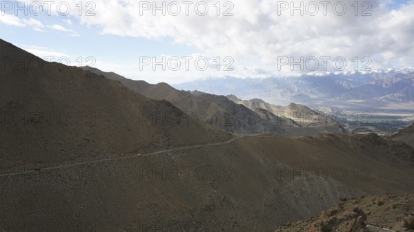 A road along a rocky mountainside that runs through a vast landscape under clear skies, trekking in