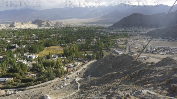 Extensive mountain and valley landscape with green trees and cloudy sky, trekking in Ladakh,