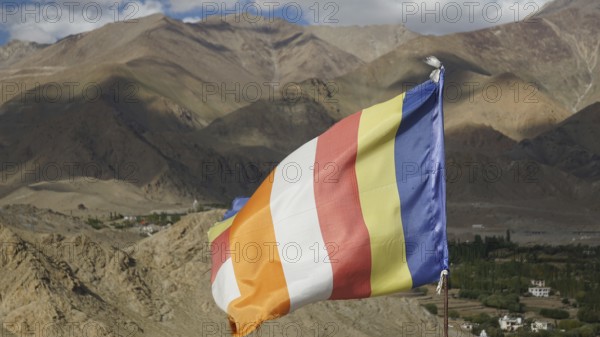 Colorful international Buddhist flag in a mountainous landscape over a green valley, Leh, trekking