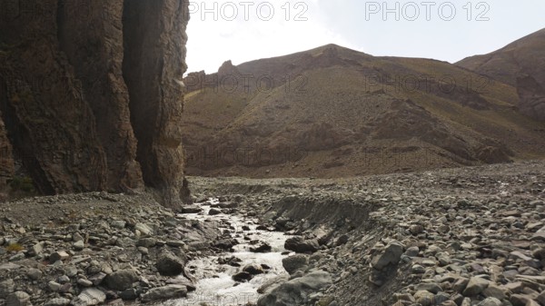 A stream flows through a dry, rocky landscape with high rock walls, trekking at Stok La Pass in