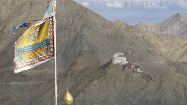 Colourful Buddhist flag with Namgyal Tsemo Buddhist monastery surrounded by mountains and sky, Leh,