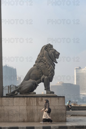 Cairo, Egypt. July 1st 2024 A woman walks past one of the famous bronze lions guarding Qasr El Nil