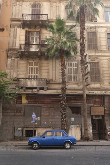 Cairo, Egypt. July 1st2024 A small blue car parked in an empty street of Downtown Cairo, with palm