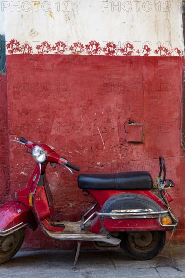 Cairo, Egypt. November 26th 2022 Cute red motor scooter parked against a red painted wall in the