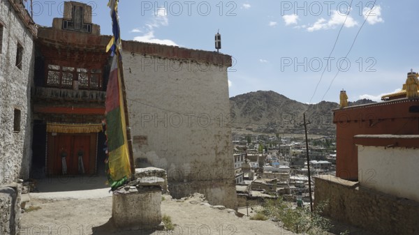 Houses and a colorful big prayer flag with mountains in the background under blue sky, Leh, city