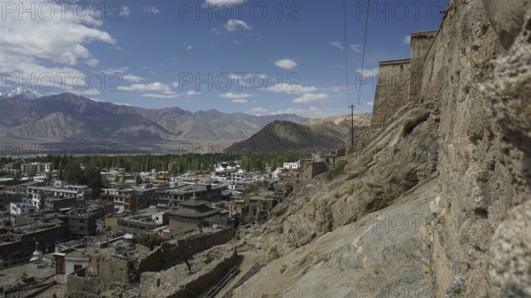 View of Leh on the mountainside with a stone wall and clouds in the sky, view from Leh Palace to