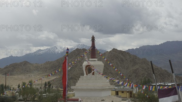 A stupa in Leh, surrounded by colorful prayer flags and mountain panorama in the background, Leh,