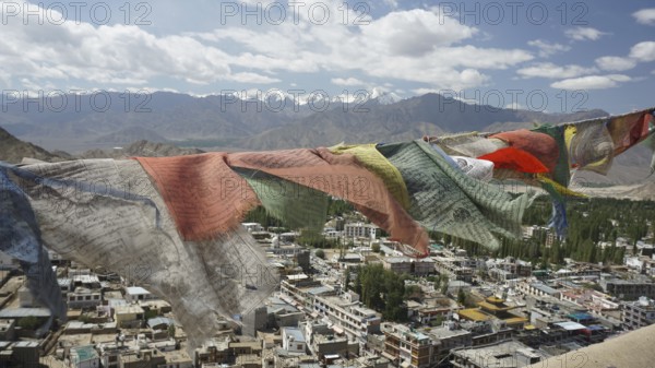 Prayer flags fly over Leh, a city with mountains and cloudy sky in the background, view from Leh