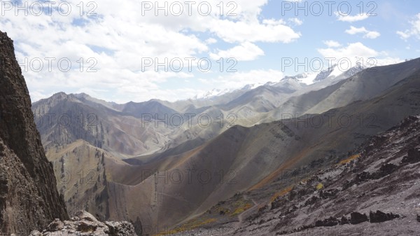 Panoramic view of a mountainous landscape with rolling hills and snow-capped peaks on the horizon,