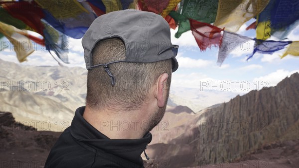Person looking at a vast mountain landscape under fluttering prayer flags, trekking at Stok La Pass