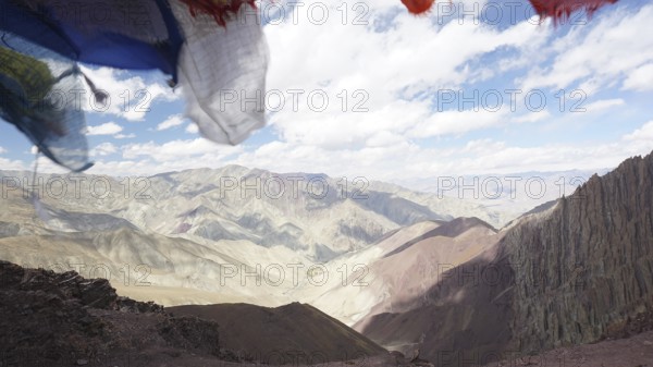 Prayer flags in front of a vast, cloud-covered mountain landscape, trekking at Stok La Pass in