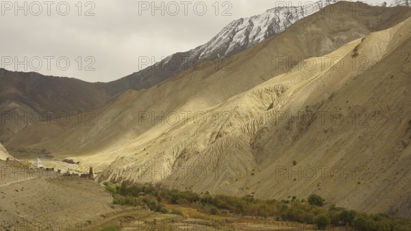 Wide valley with dramatic, barren mountain landscapes under cloudy sky, trekking in Ladakh,