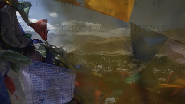 Colourful prayer flags fly against a vast mountain landscape and blue sky with clouds, Ladakh,