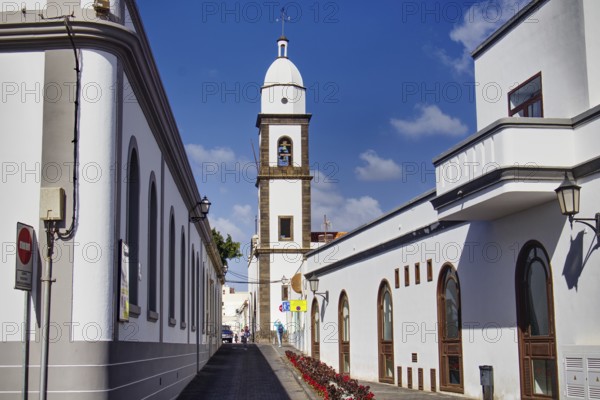 White buildings with church tower of the Iglesia de San Ginés church along a paved street under