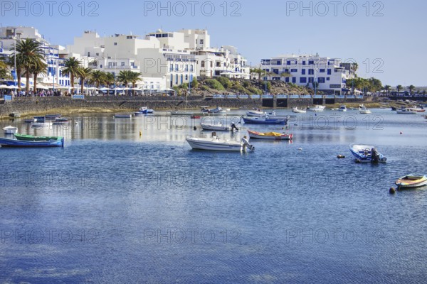 Blue water with boats in the Charco de San Ginés lagoon in front of a coastal town with palm trees