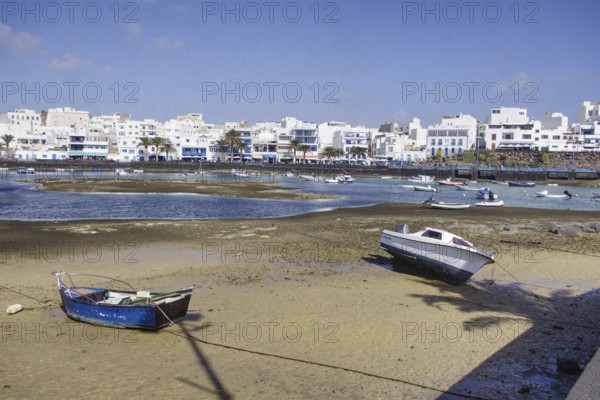 Boats on the banks of Charco de San Ginés lagoon in front of white buildings under blue sky,