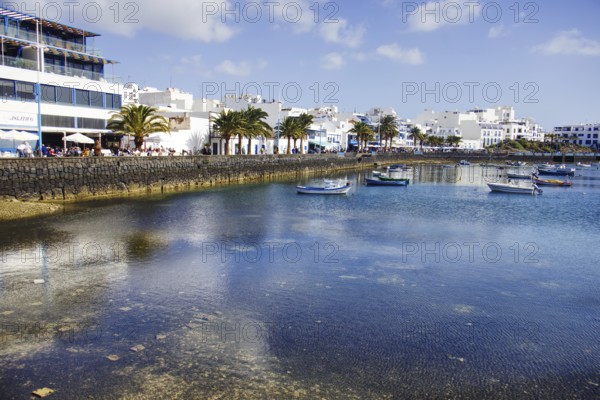 Boats on the calm waters of the Charco de San Ginés lagoon surrounded by palm trees and white