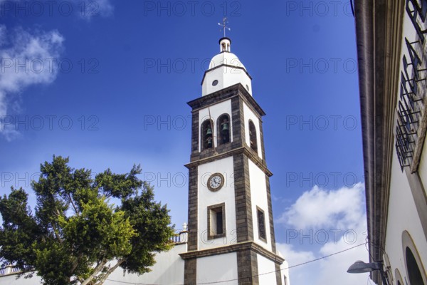 White church tower with clock of the Iglesia de San Ginés church under blue sky, surrounded by
