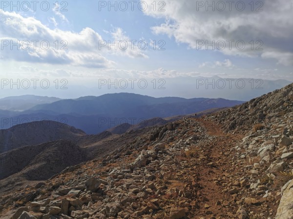 Rocky mountain trail with views of surrounding mountains and clouds, climbing Tahtali Dagi, Lycia,