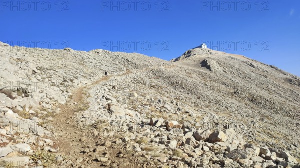 A trail snakes over a rocky mountainside up to the summit of Tahtali with clear skies, climbing