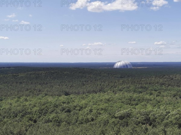 View of an extensive forest with the dome of Tropical Island, Cargolifter Hall on the horizon under