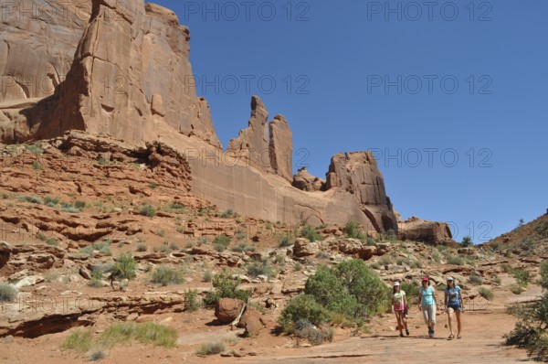 Several people are hiking in a dry, rocky landscape called Wall Street, under a bright blue sky,