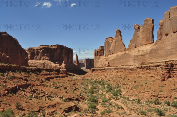 A wide valley with imposing sandstone cliffs, called Wall Street, under a bright blue sky, Arches