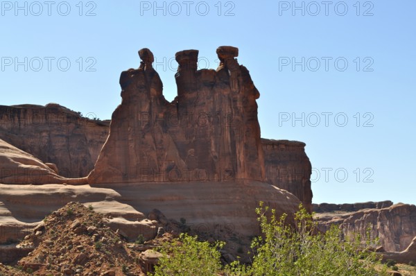 Three Gossips, a majestic red sandstone rock formation rising above a bright blue sky, Arches