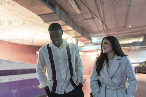 Diverse couple happily walking through an underground car park, enjoying their date while having a