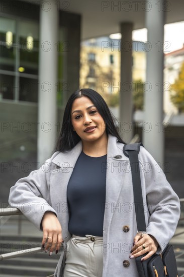 Confident indian woman showing her elegant business casual style, leaning on a railing in an urban